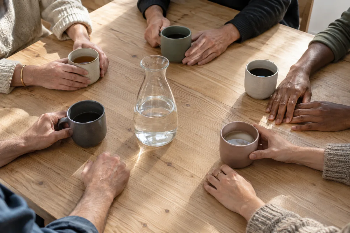 Mains de plusieurs personnes posées autour de tasses sur une grande table en bois